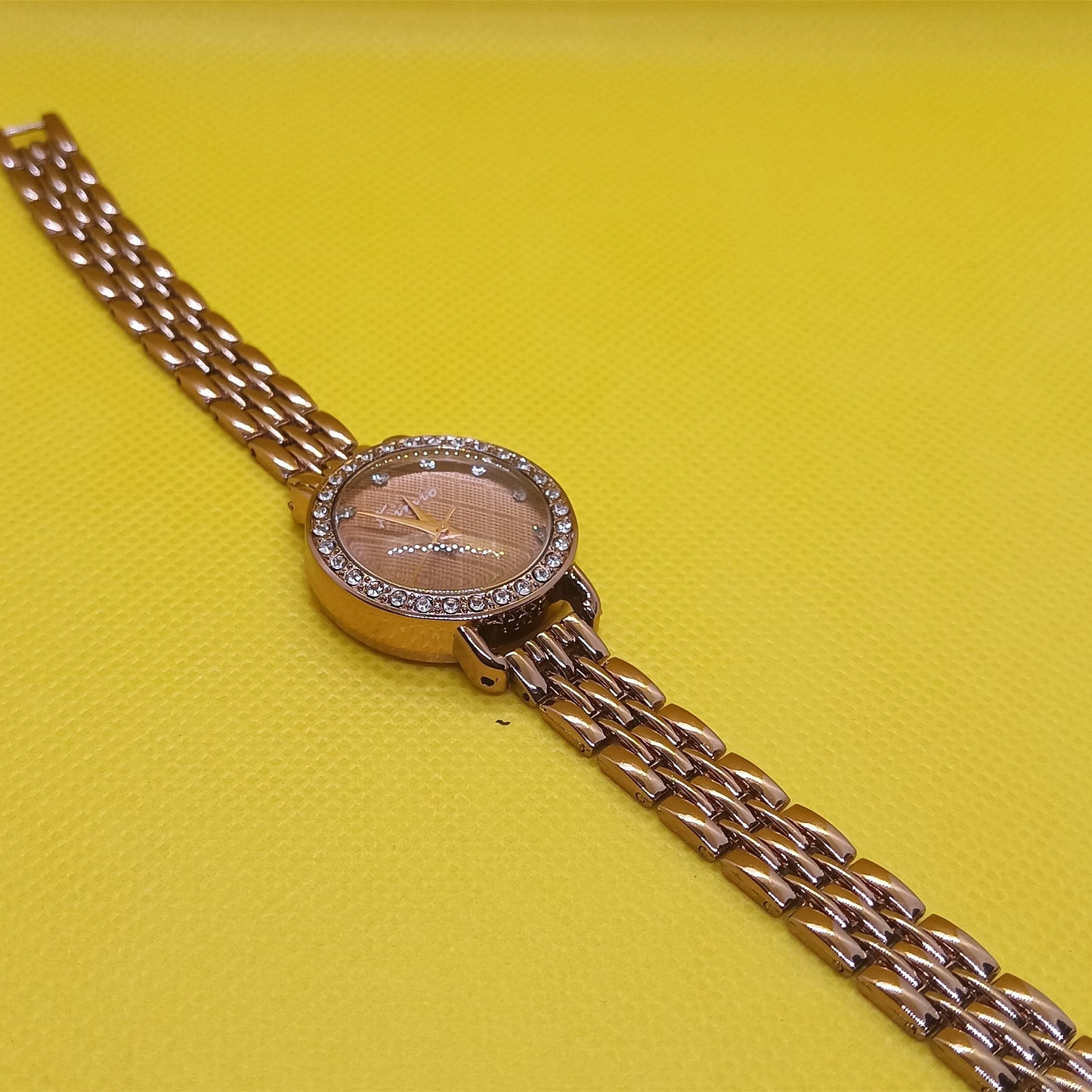 Gold wristwatch with a pink face on a yellow background