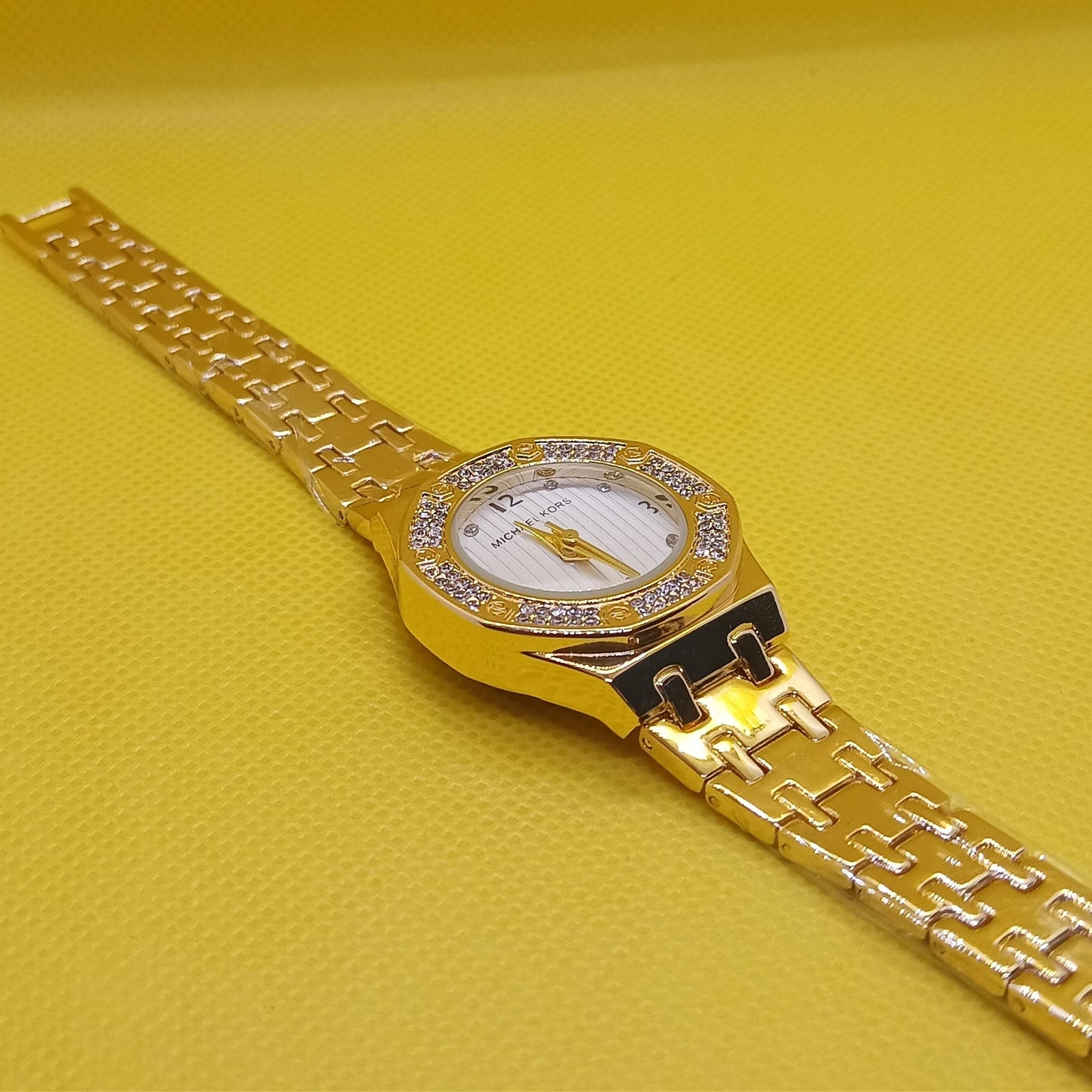 Gold wristwatch with diamond-studded face on a yellow background