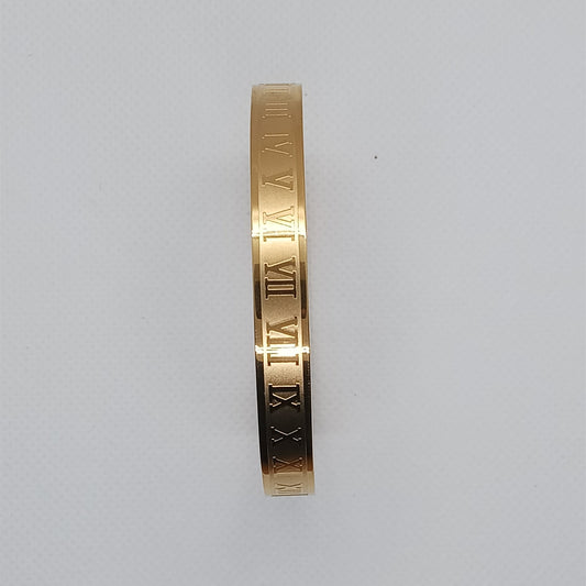 Gold bracelet with Roman numeral engraving on a light gray background