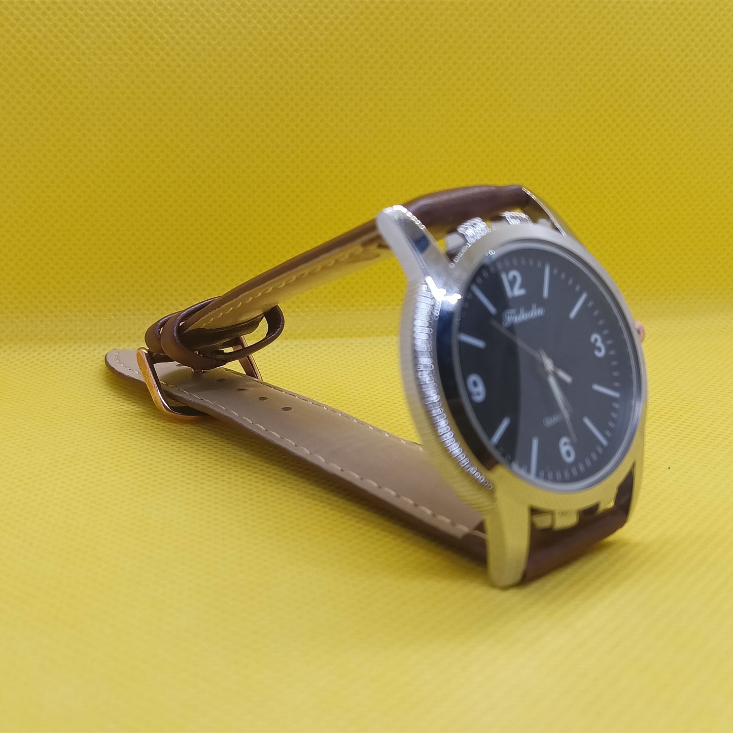 Watch with a black face and brown strap on a yellow background