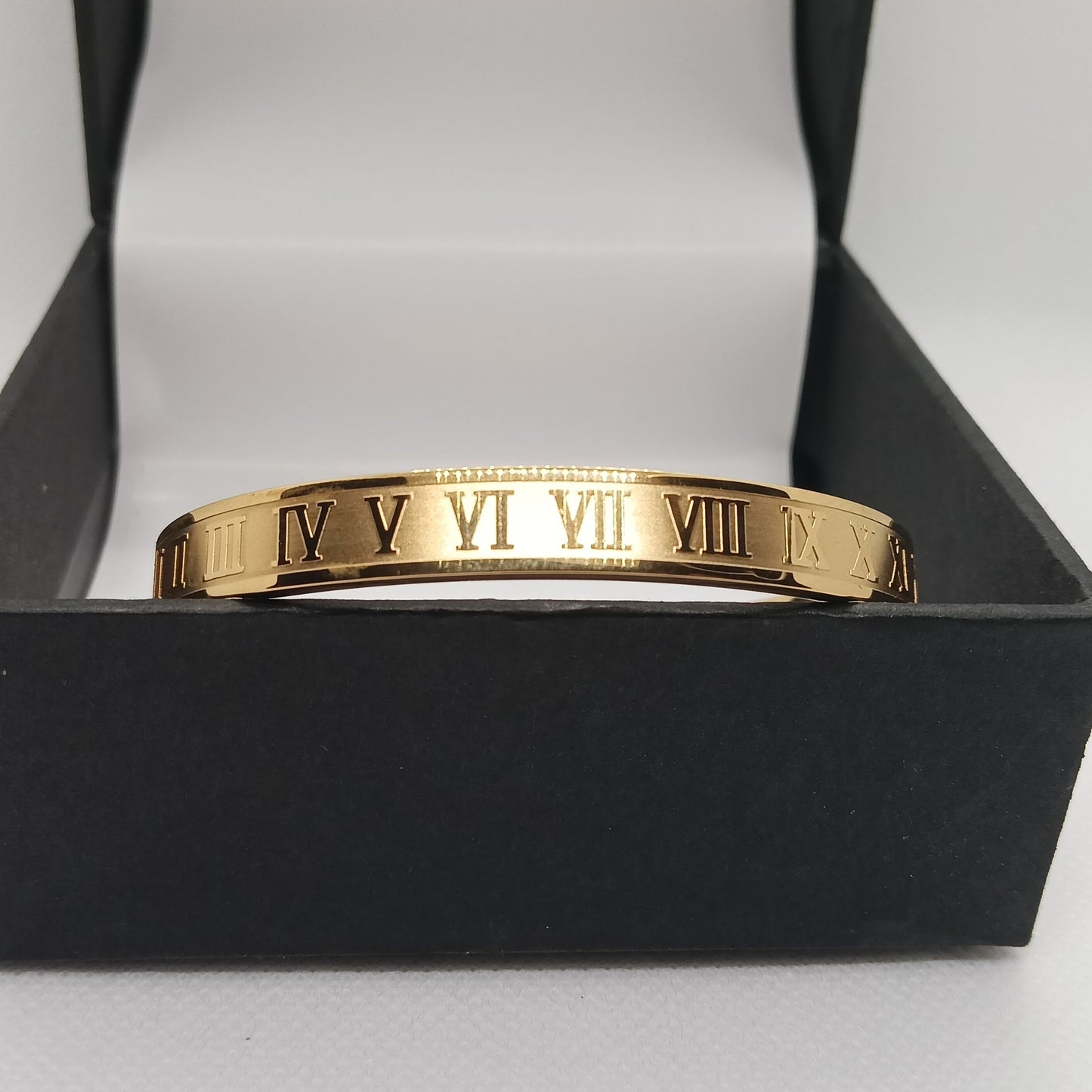 Gold bracelet with Roman numeral design in a black box on a white background