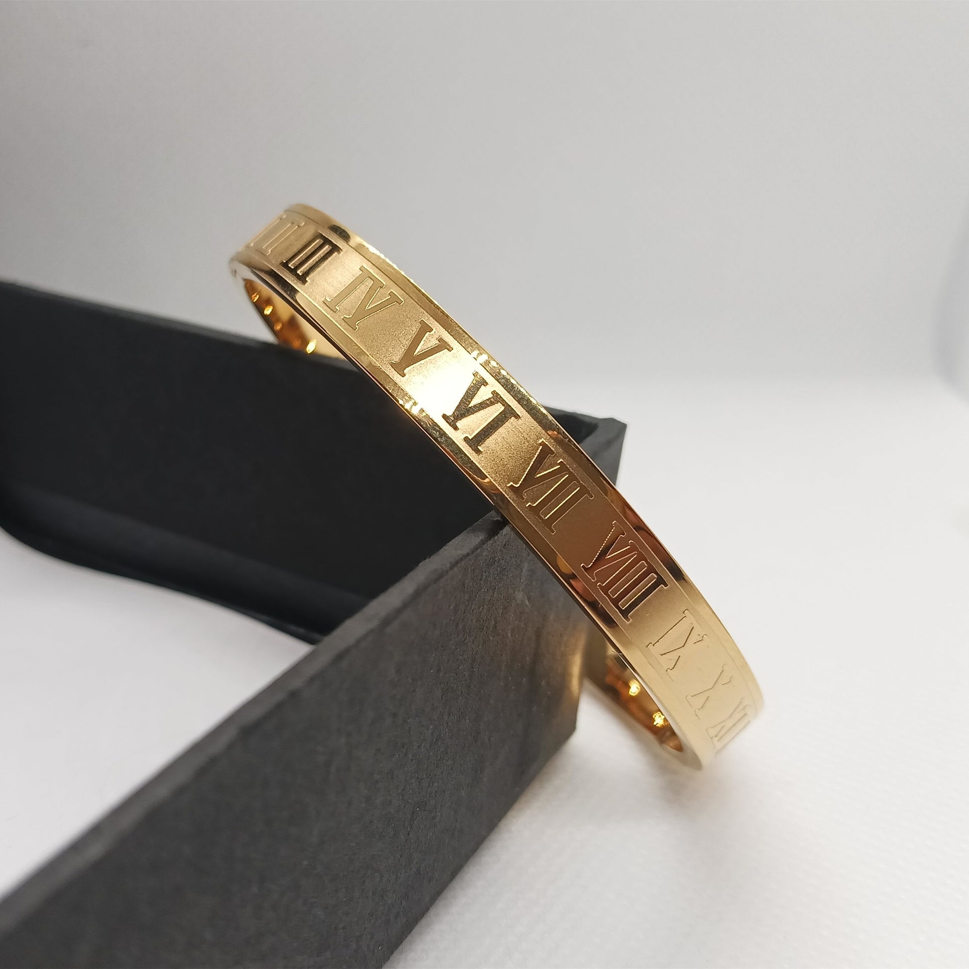 Gold bracelet with Roman numeral design on a white background