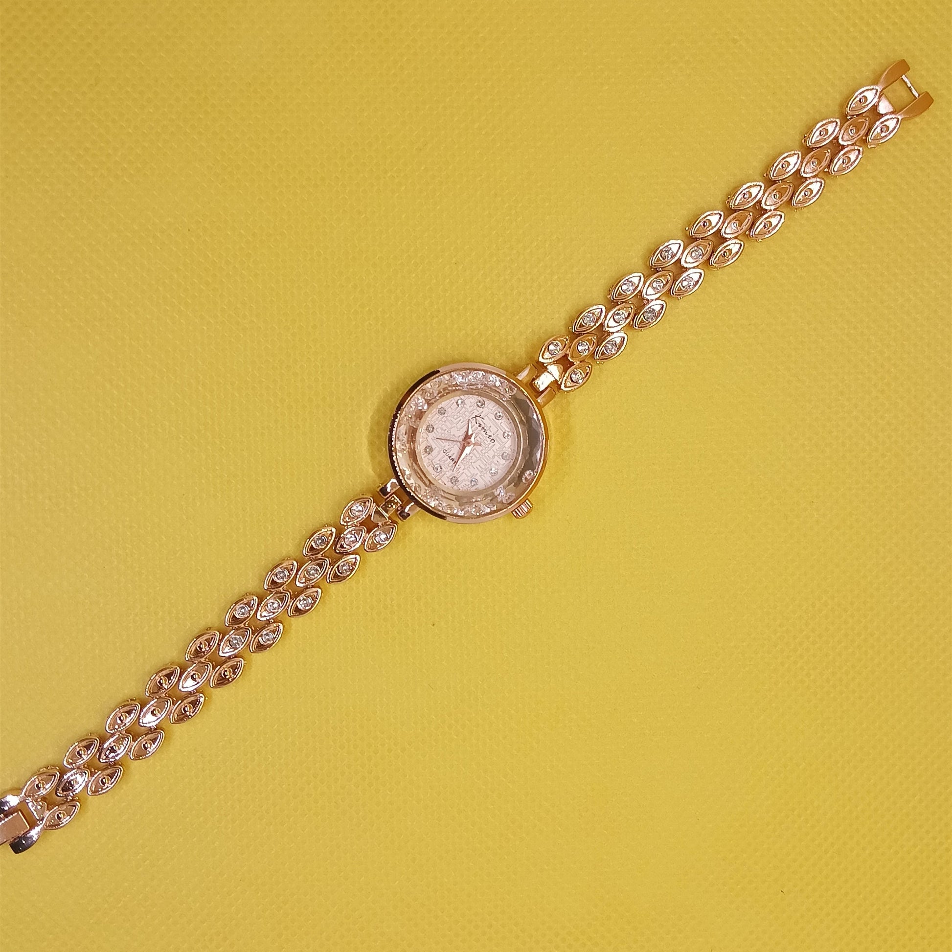 Gold wristwatch with a chain strap on a yellow background