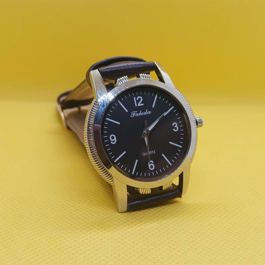 Wristwatch with black face and leather strap on a yellow background