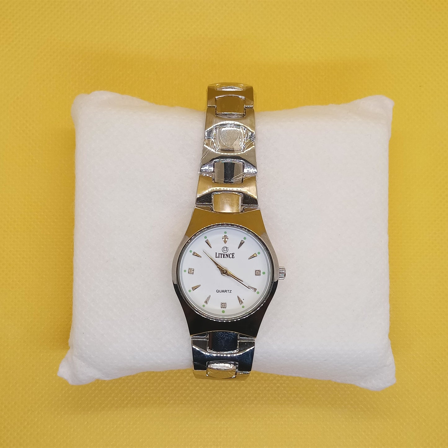 Silver watch on a white cushion against a yellow background
