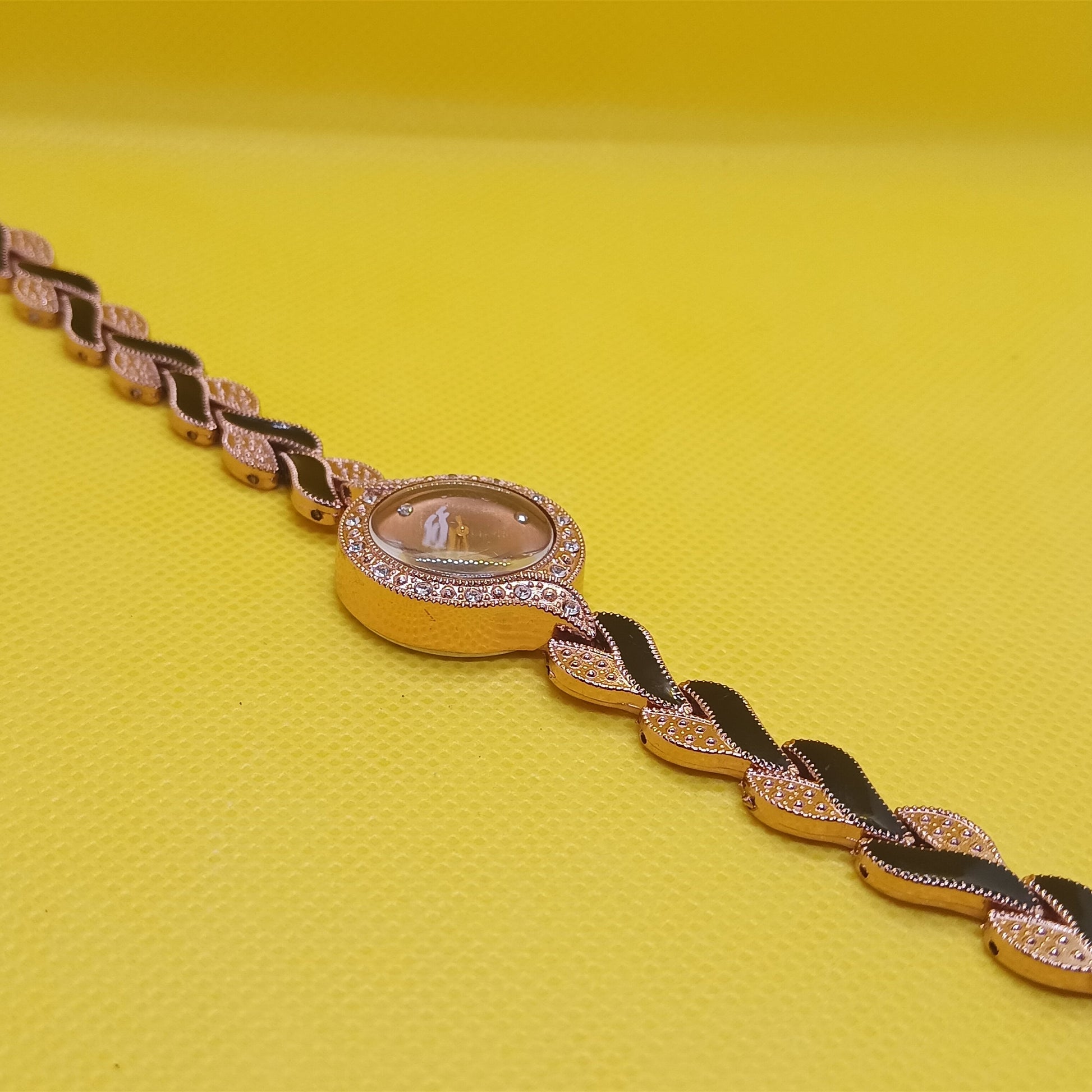 Gold bracelet with a central gemstone on a yellow background
