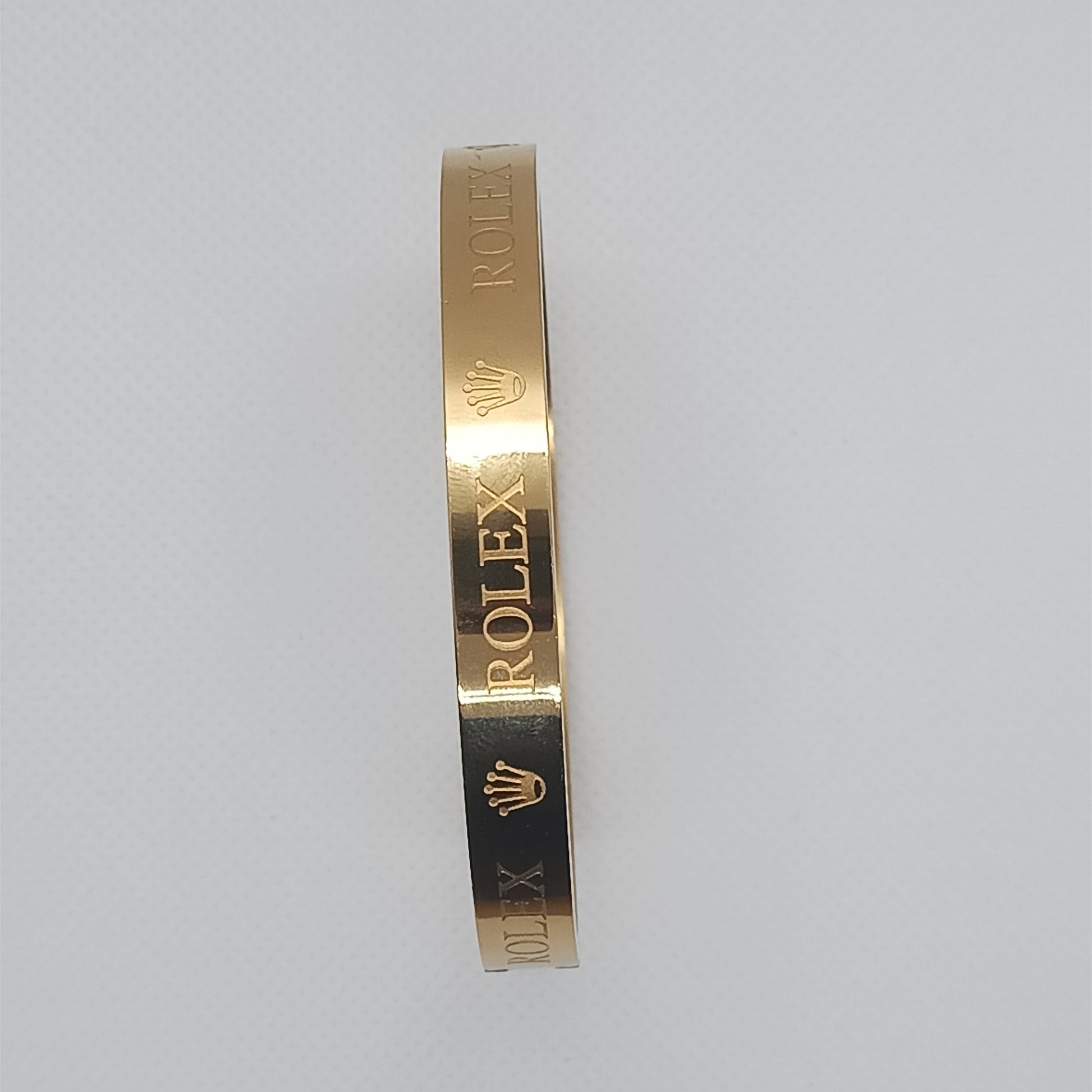 Gold bracelet with 'Rolex' engraving on a light gray background