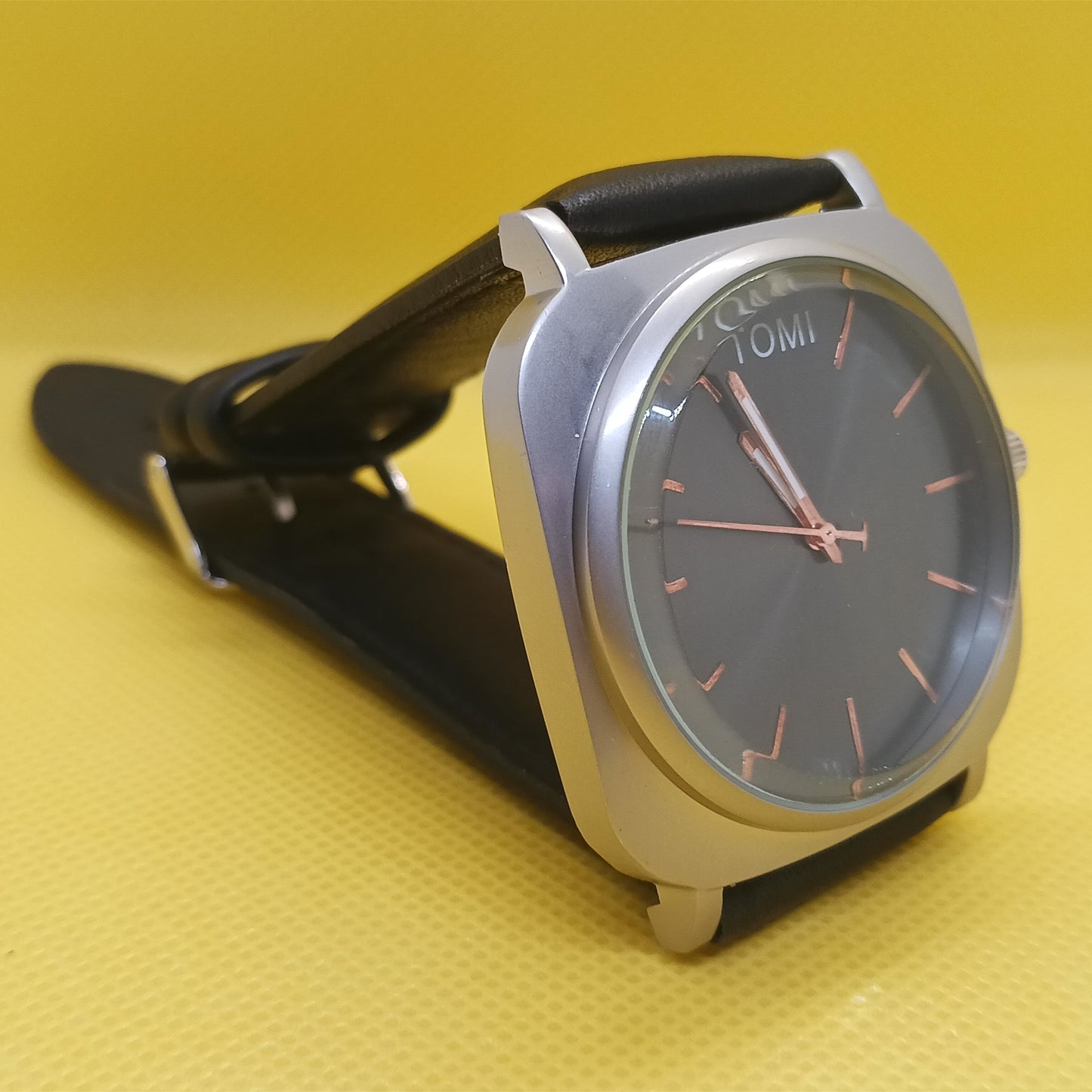 Watch with black strap and silver case on a yellow background