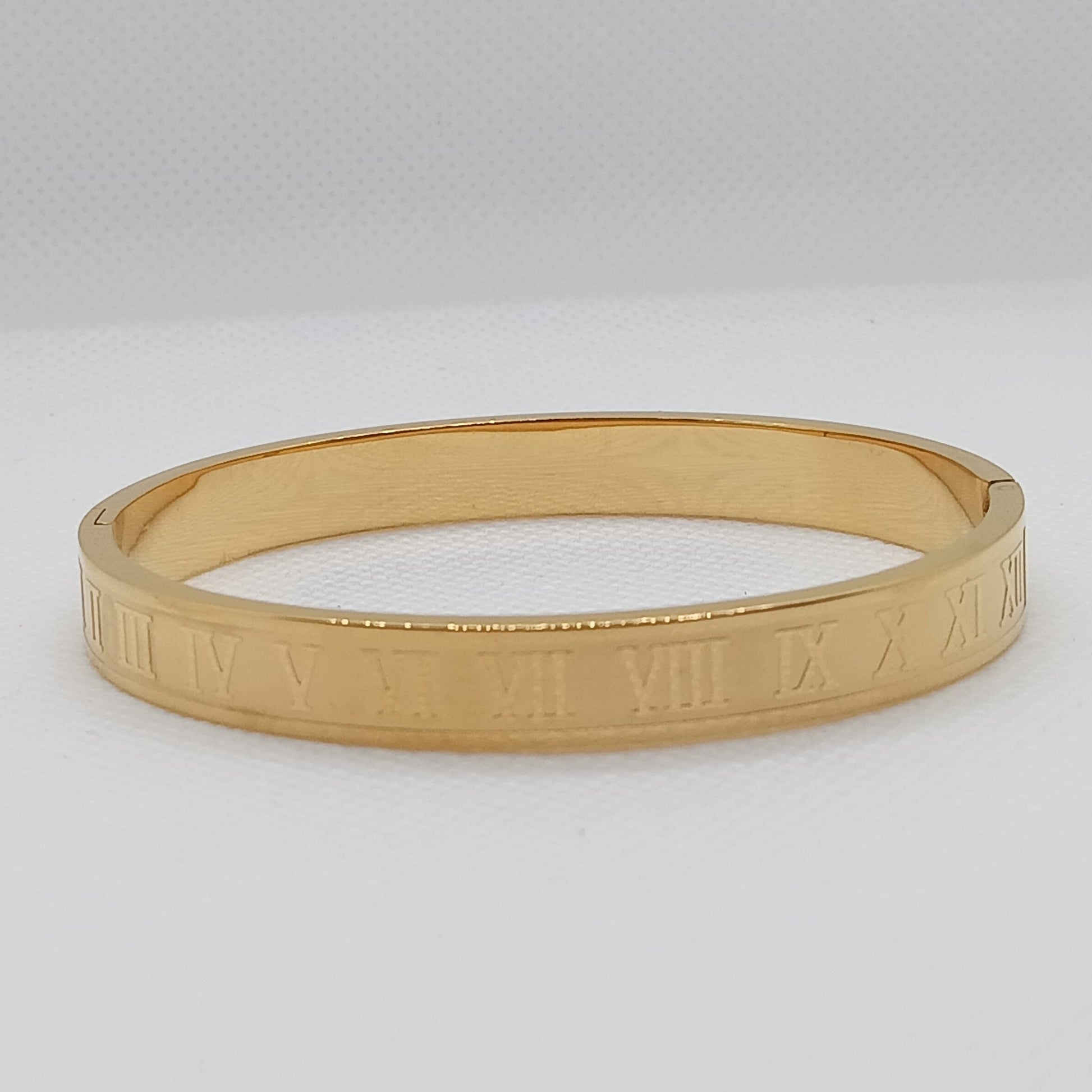 Gold bangle with Roman numeral design on a light gray background