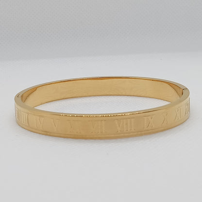 Gold bangle with Roman numeral design on a light gray background