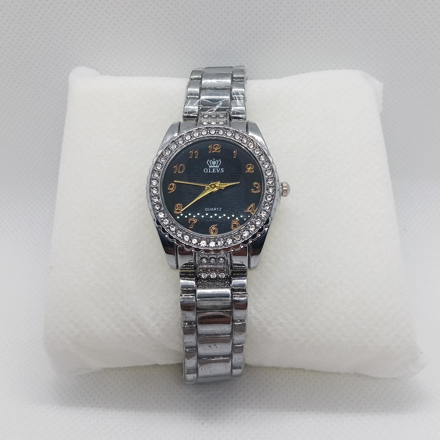 Silver watch with a black face on a white cushion against a light gray background