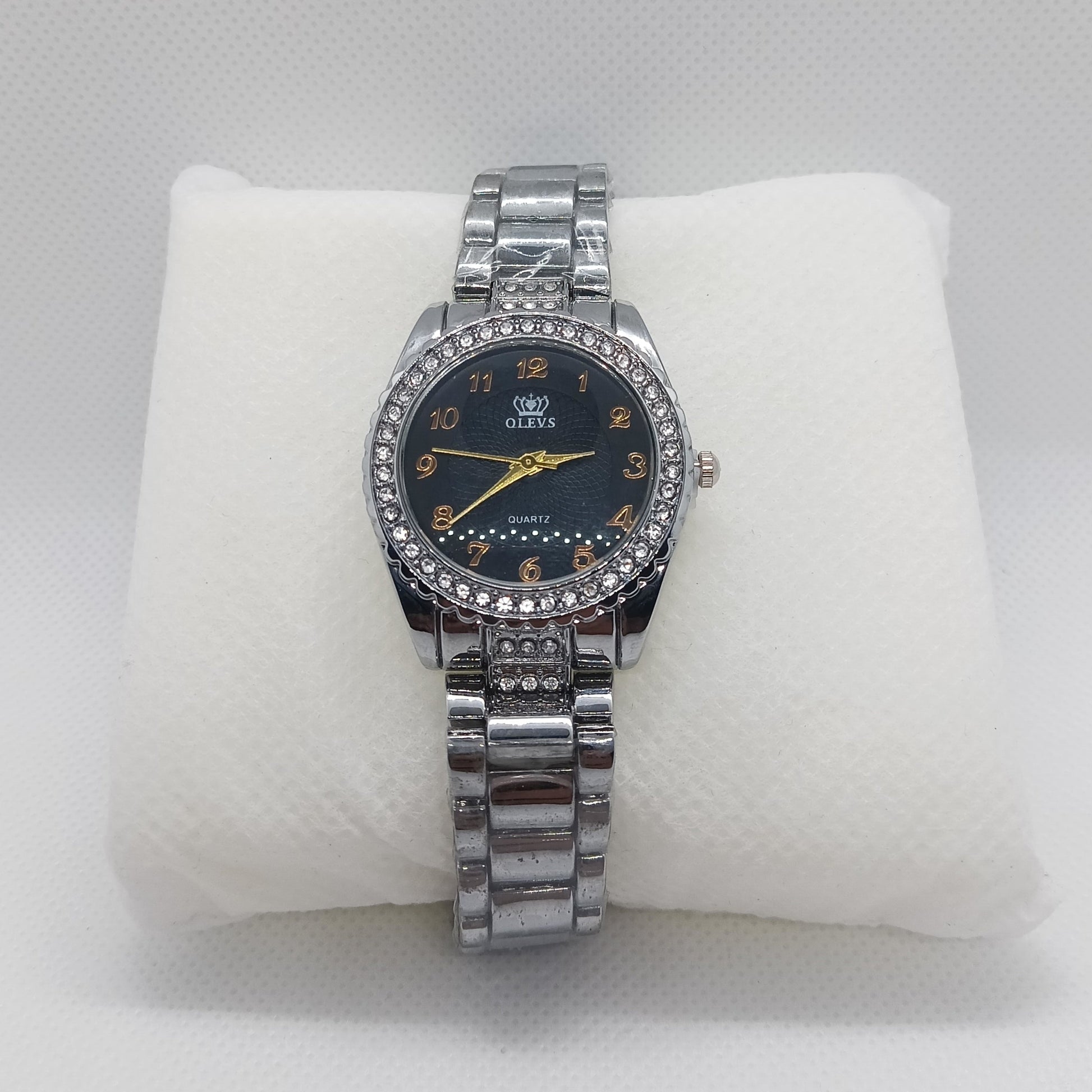Silver watch with a black face on a white cushion against a light gray background