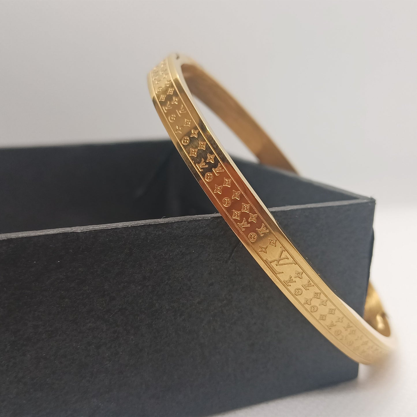 Gold bracelet with intricate designs on a dark gray box