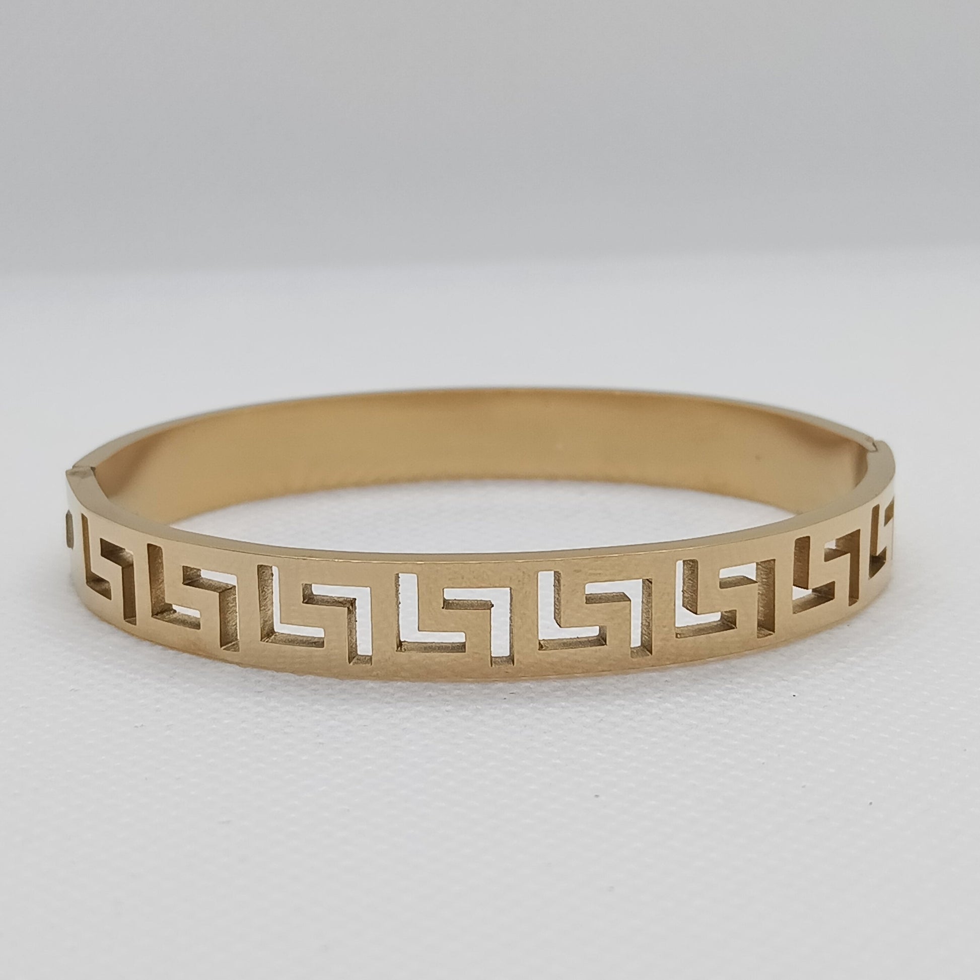 Gold bracelet with geometric pattern on a light gray background