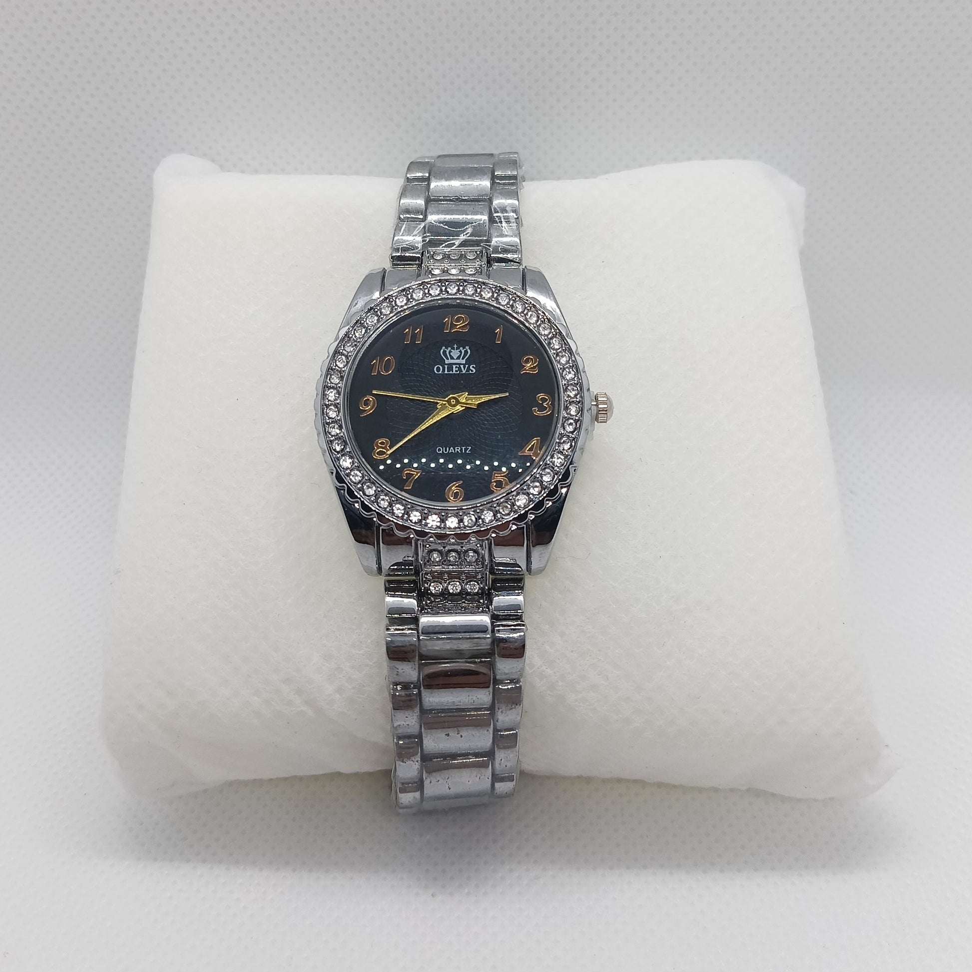 Silver watch with a black face on a white cushion against a light gray background