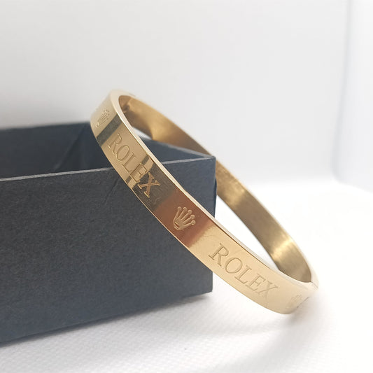 Gold Rolex bracelet on a white surface with a gray box in the background