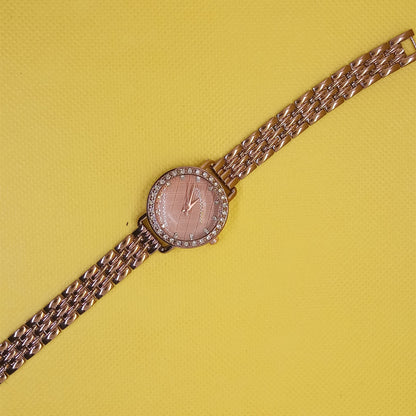 Gold wristwatch with a pink face on a yellow background