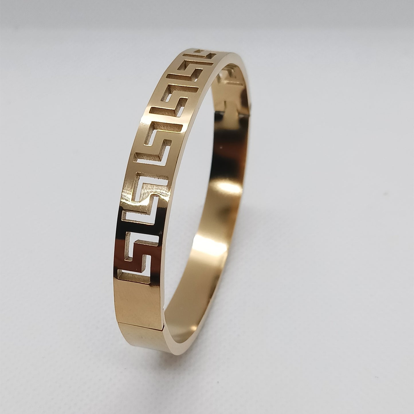 Gold bracelet with a geometric pattern on a light gray background