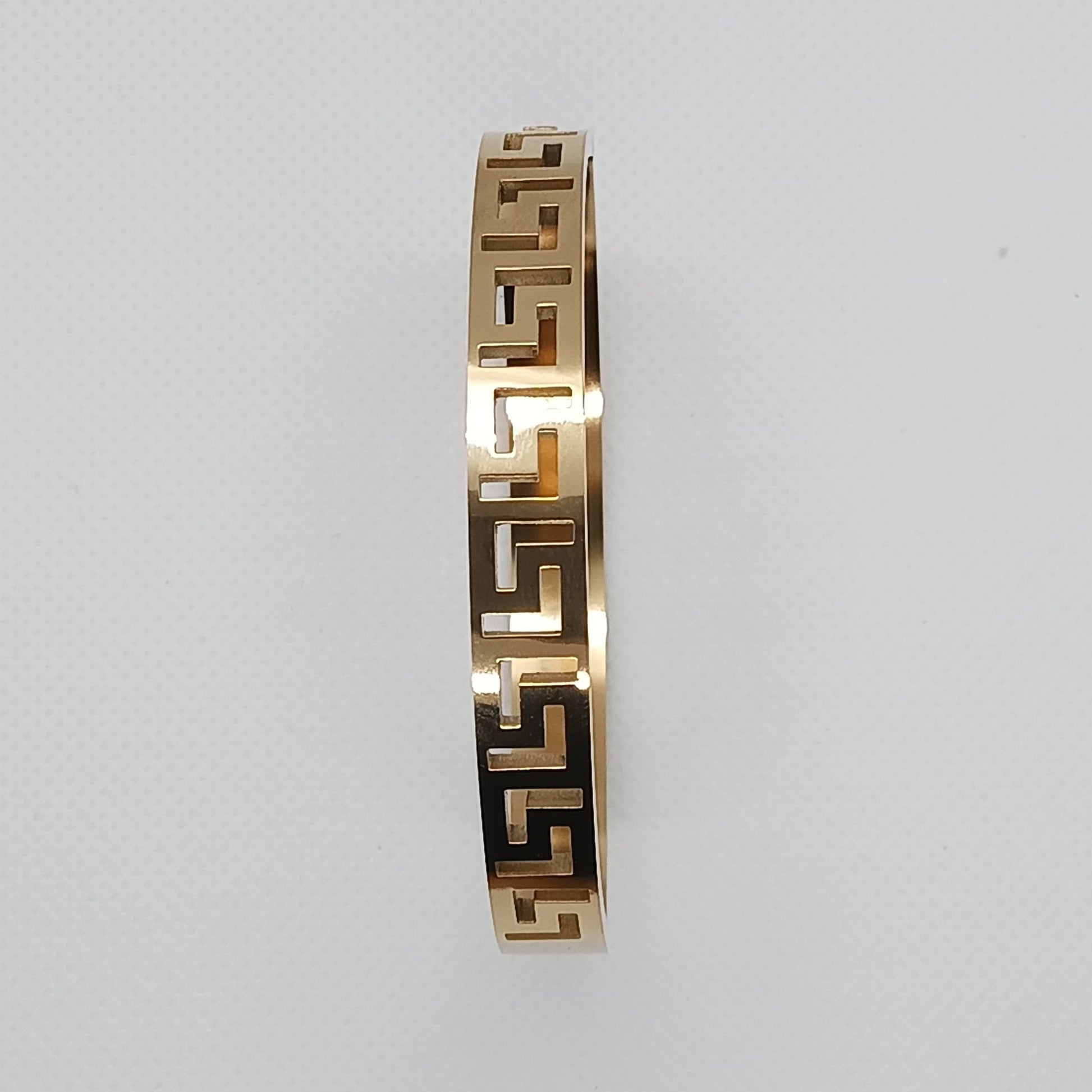 Gold bracelet with a geometric pattern on a light gray background