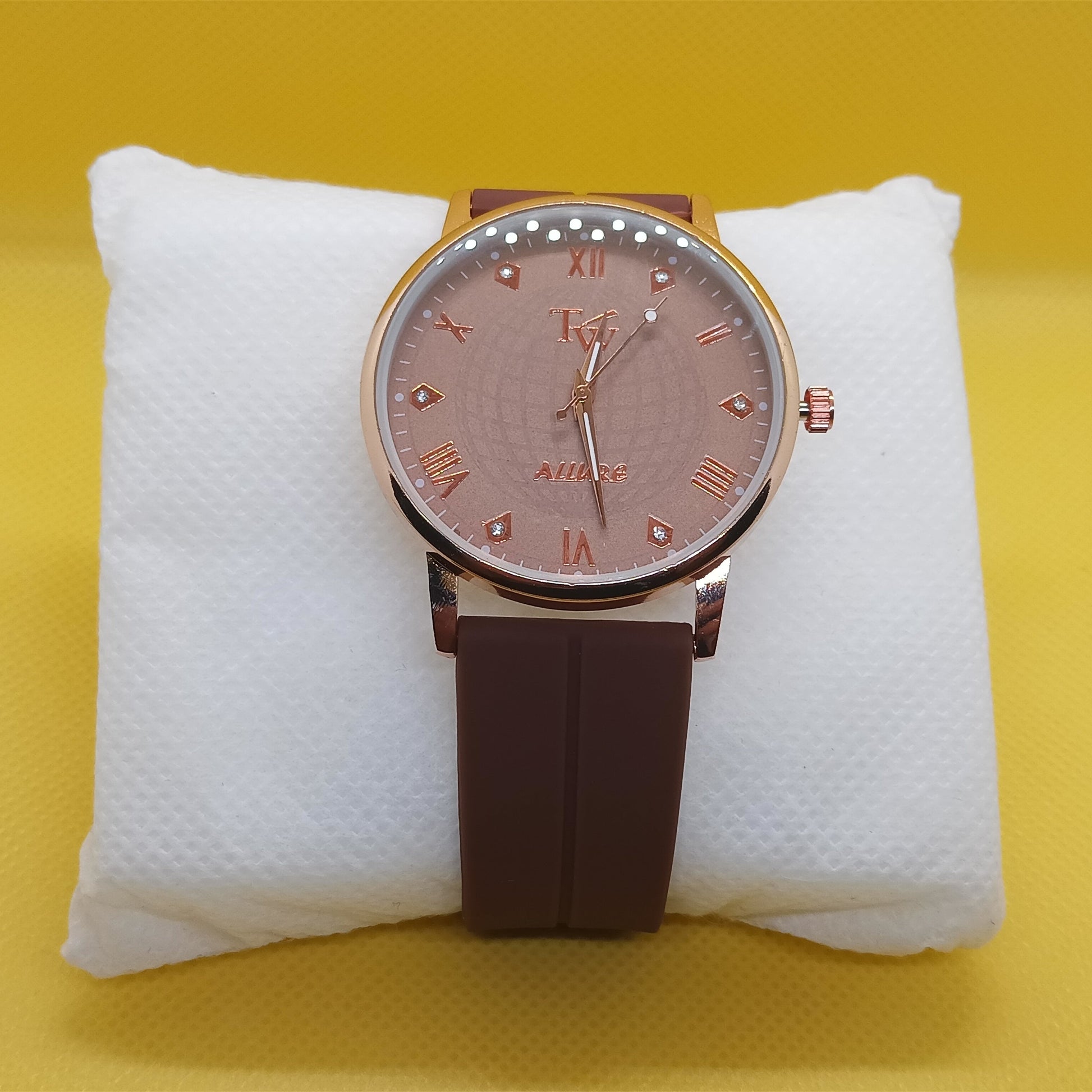 Watch with brown strap and pinkish dial on a white cushion against a yellow background