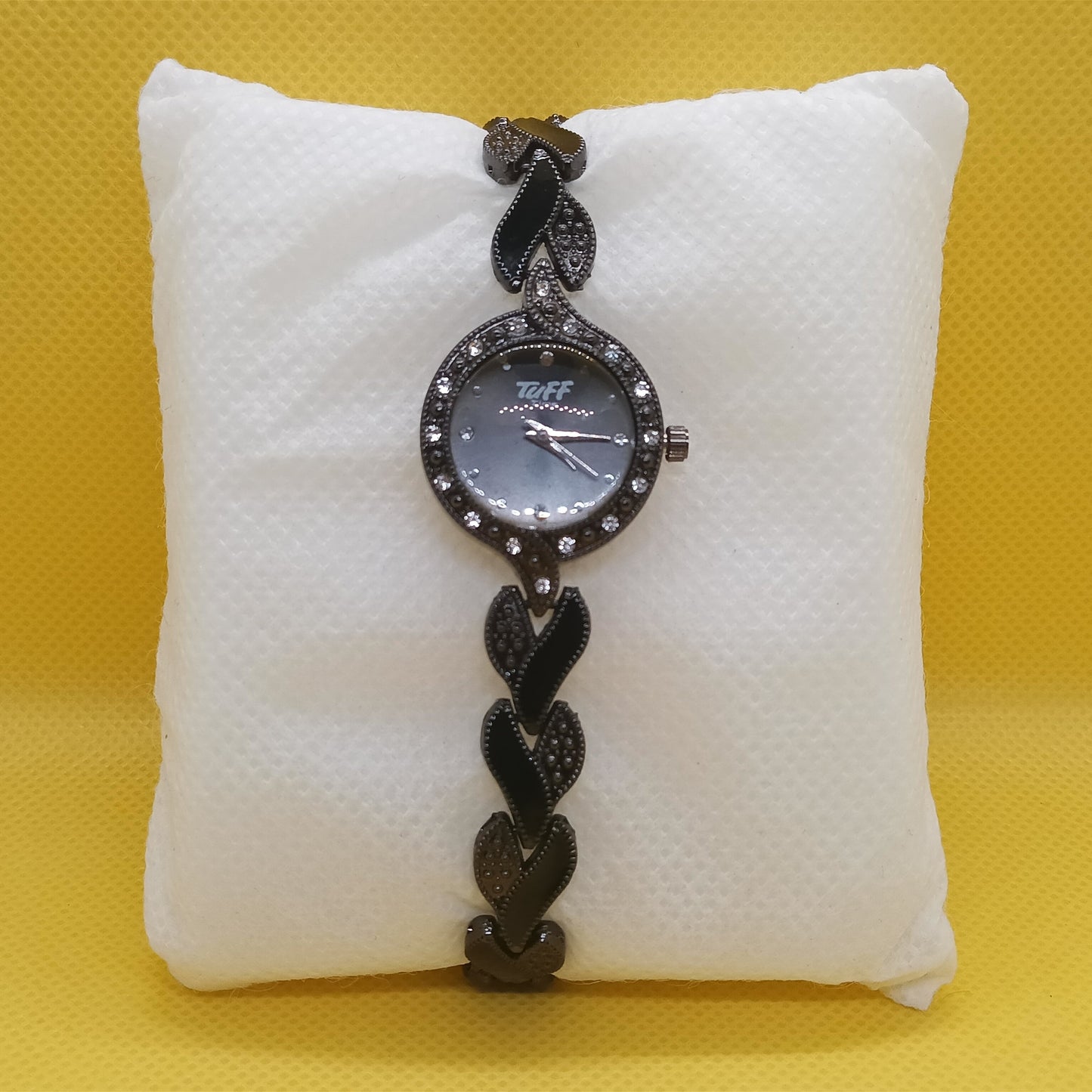 Black braided watch on a white cushion against a yellow background
