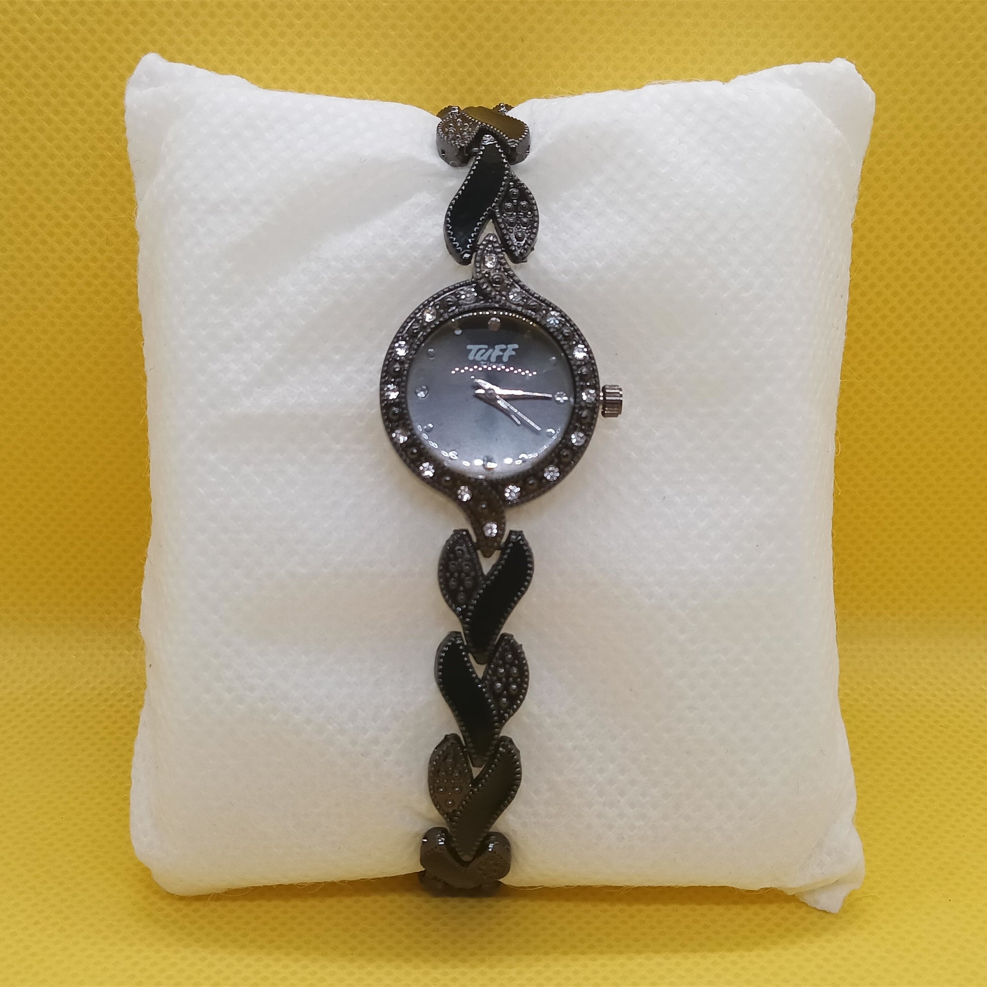 Black braided watch on a white cushion against a yellow background