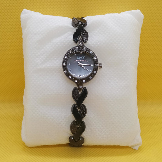 Black braided watch on a white cushion against a yellow background