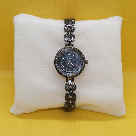 Wristwatch with decorative band on a white cushion against a yellow background