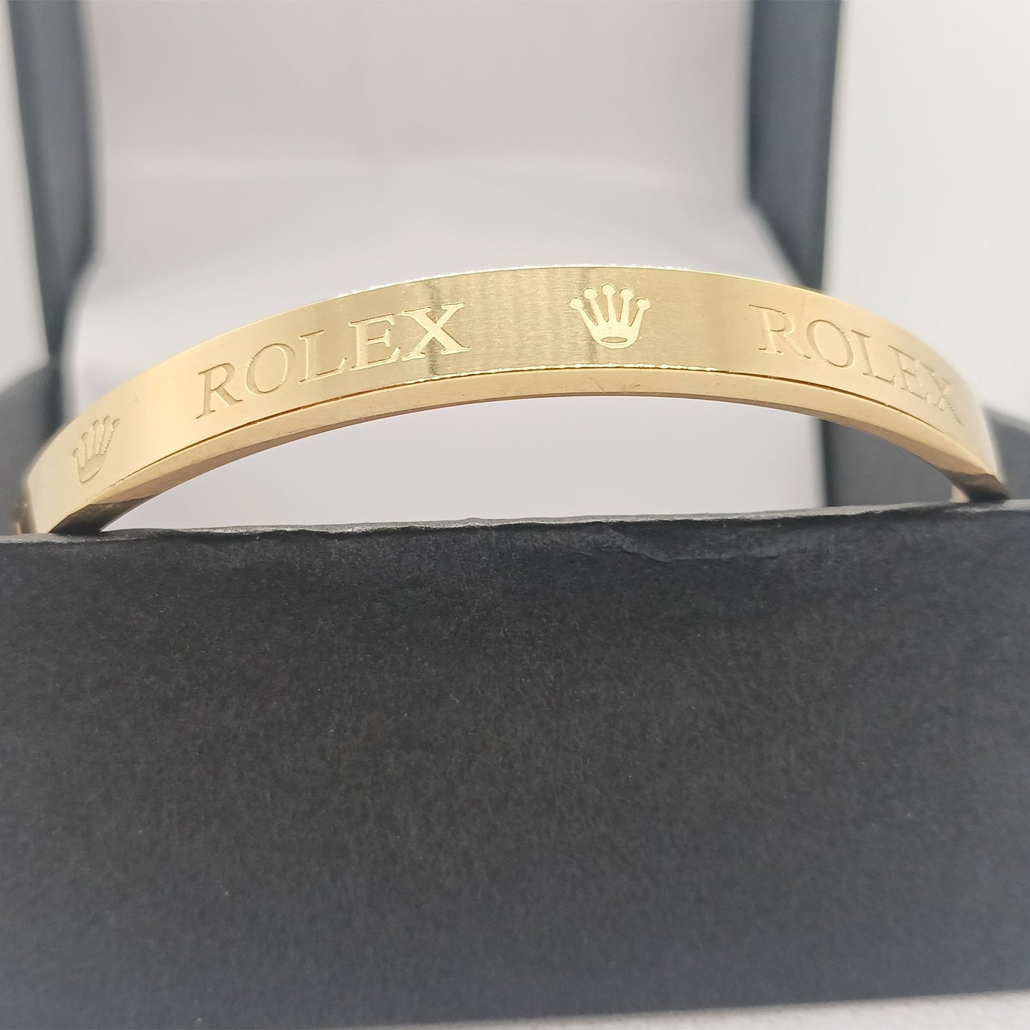 Gold bracelet with Rolex engraving on a gray background