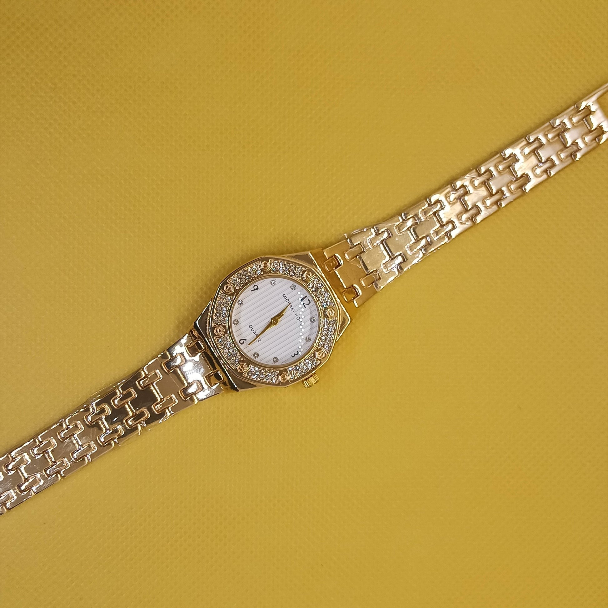 Gold wristwatch with diamond-studded face on a yellow background