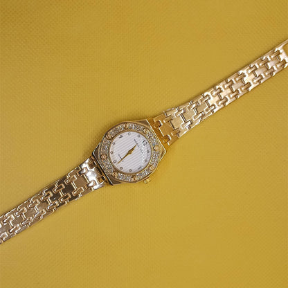 Gold wristwatch with diamond-studded face on a yellow background