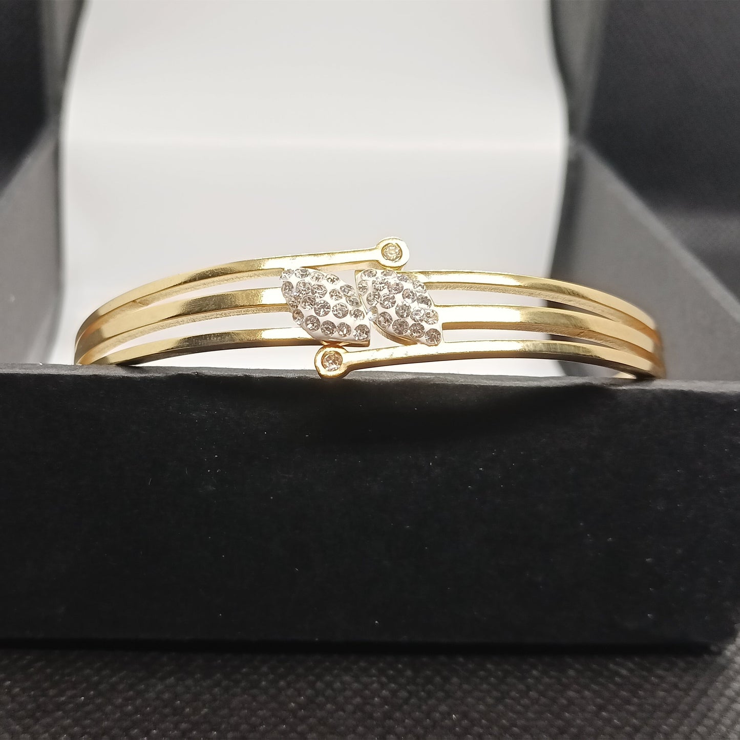 Gold bracelet with a decorative clasp on a black stand.