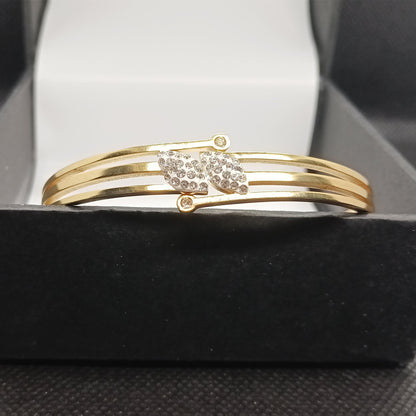 Gold bracelet with a decorative clasp on a black stand.