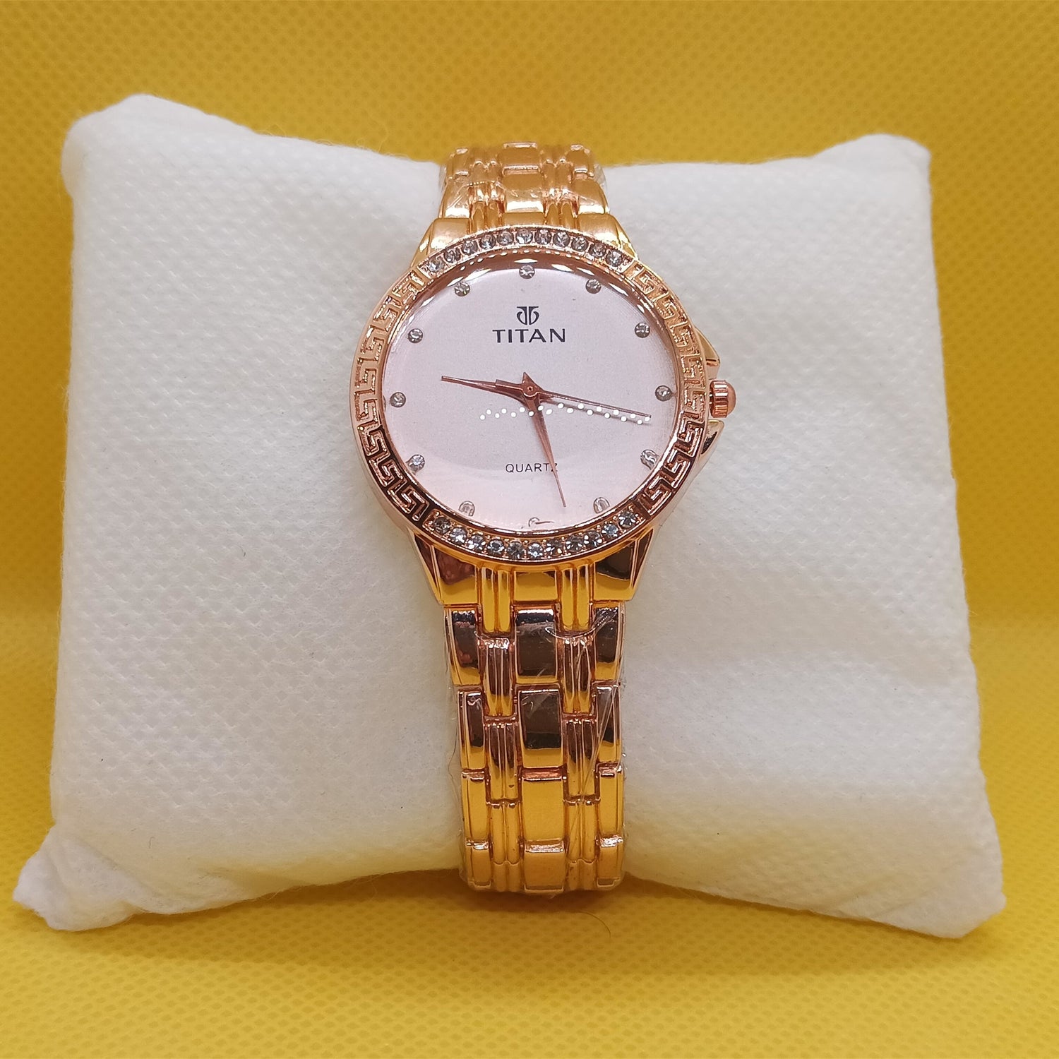 Gold Titan watch on a white cushion with a yellow background