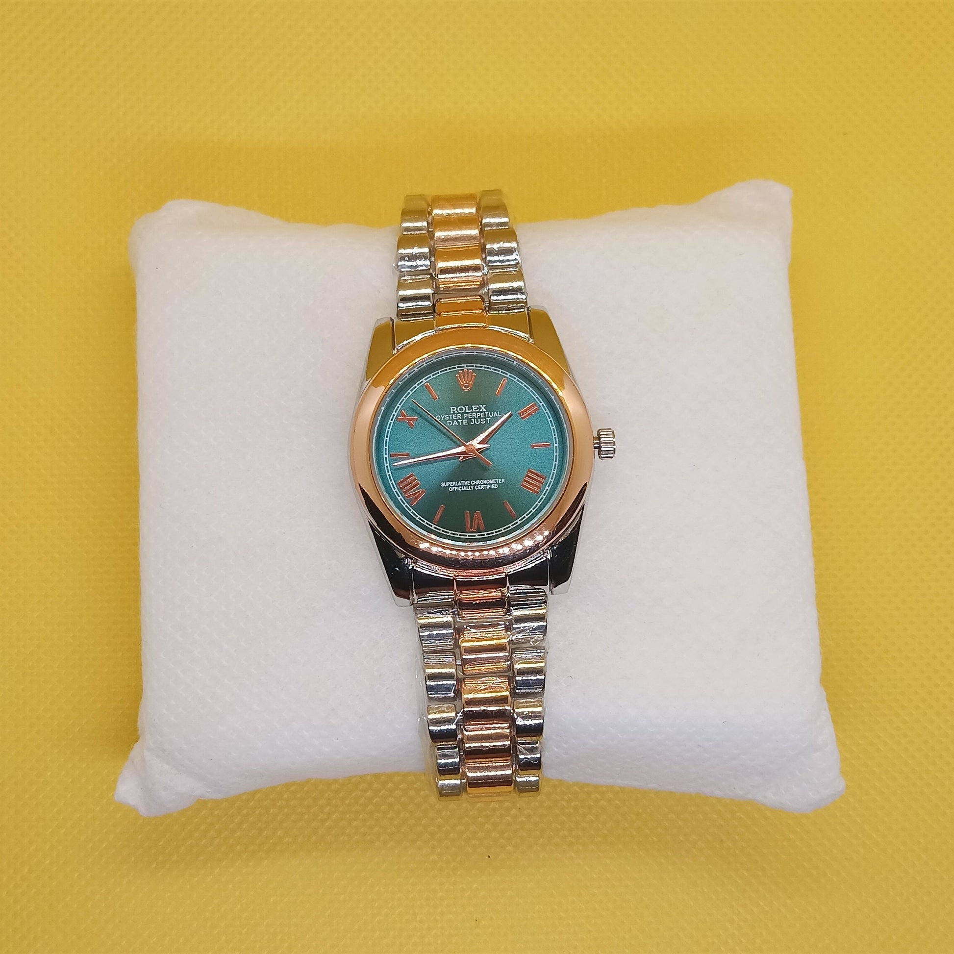 Wristwatch with a green face and gold band on a white cushion against a yellow background